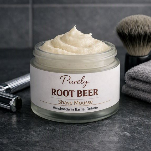 Purely Root Beer Shave Mousse — open frosted jar on dark slate bathroom counter with chrome razor, black shaving brush, and gray towel, cool masculine lighting, handmade in Barrie Ontario.