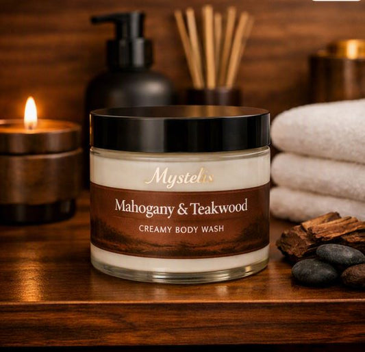 Mystelis Mahogany & Teakwood Creamy Body Wash jar filled with off‑white creamy body wash on a warm mahogany spa shelf, surrounded by candlelight, wood accents, white towels, and soft smoky teakwood elements.