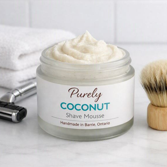 Purely Coconut Shave Mousse — creamy whipped shave mousse jar beside razor, shaving brush, and folded towel in a clean bathroom setting, handmade in Barrie Ontario.