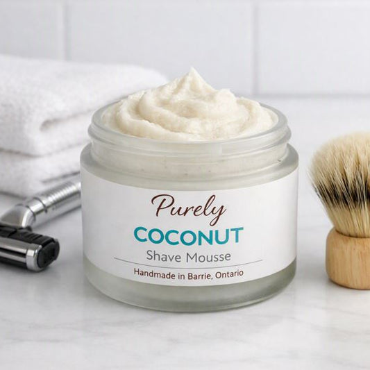 Purely Coconut Shave Mousse — creamy whipped shave mousse jar beside razor, shaving brush, and folded towel in a clean bathroom setting, handmade in Barrie Ontario.