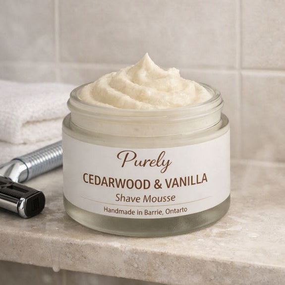 Purely Cedarwood & Vanilla Shave Mousse — creamy whipped shave mousse jar on a tiled shower shelf beside chrome razor and folded washcloth, warm neutral spa‑style lighting, handmade in Barrie Ontario.