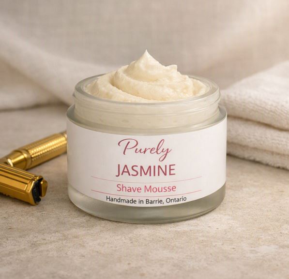 Purely Jasmine Shave Mousse — open frosted jar on matte stone surface with gold razor and linen backdrop, soft floral spa‑style lighting, handmade in Barrie Ontario.