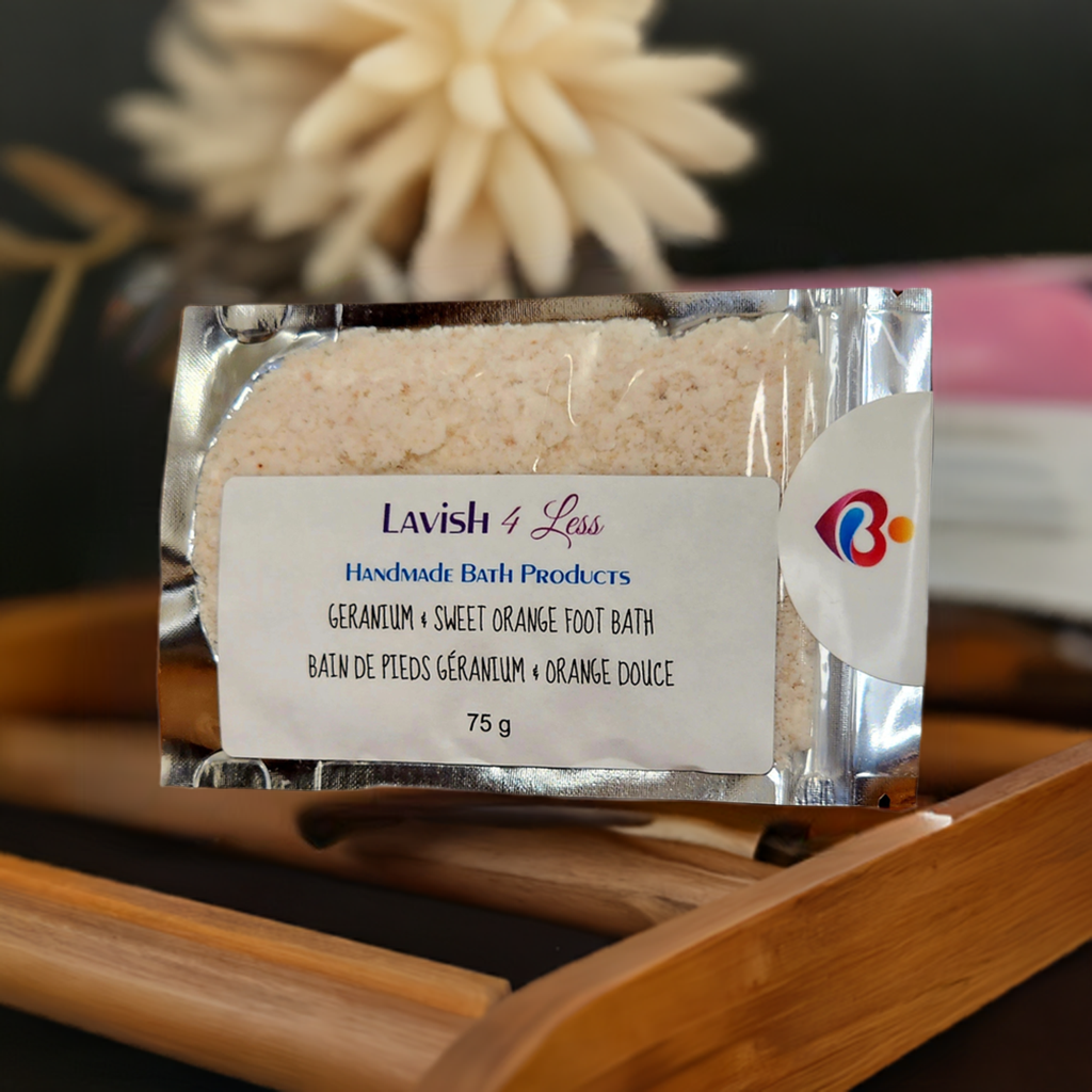 Geranium and sweet orange foot bath salts in clear packaging displayed on a wooden surface with floral and citrus accents.