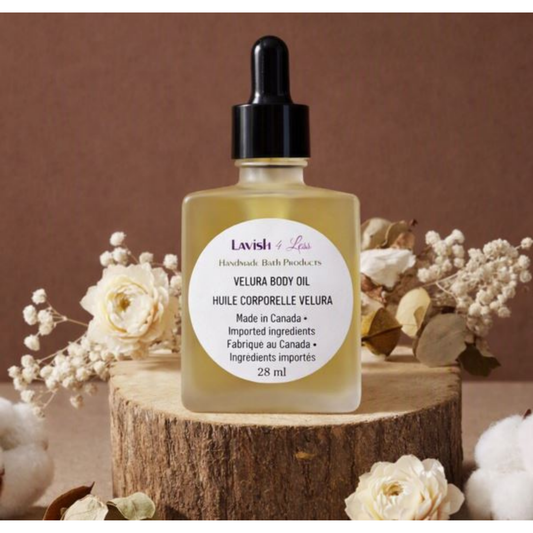 Lavish 4 Less Velura Body Oil — handmade bath product in a frosted glass bottle with a black dropper cap, placed on a wooden base surrounded by dried flowers and cotton against a warm brown background.